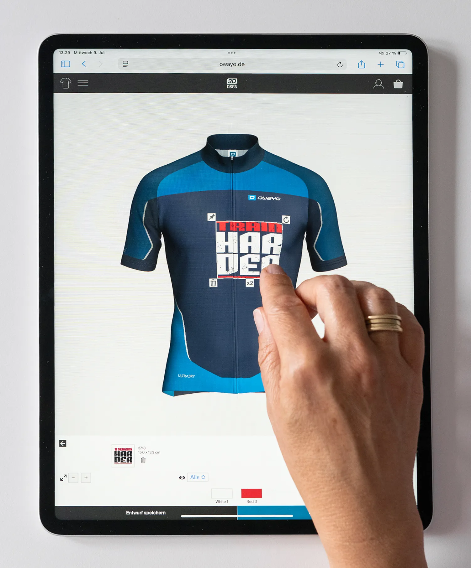 A hand interacts with a tablet displaying the Champion Export Import website, showing a custom-designed blue and dark blue cycling jersey with the text 'TRAIN HARDER'.
